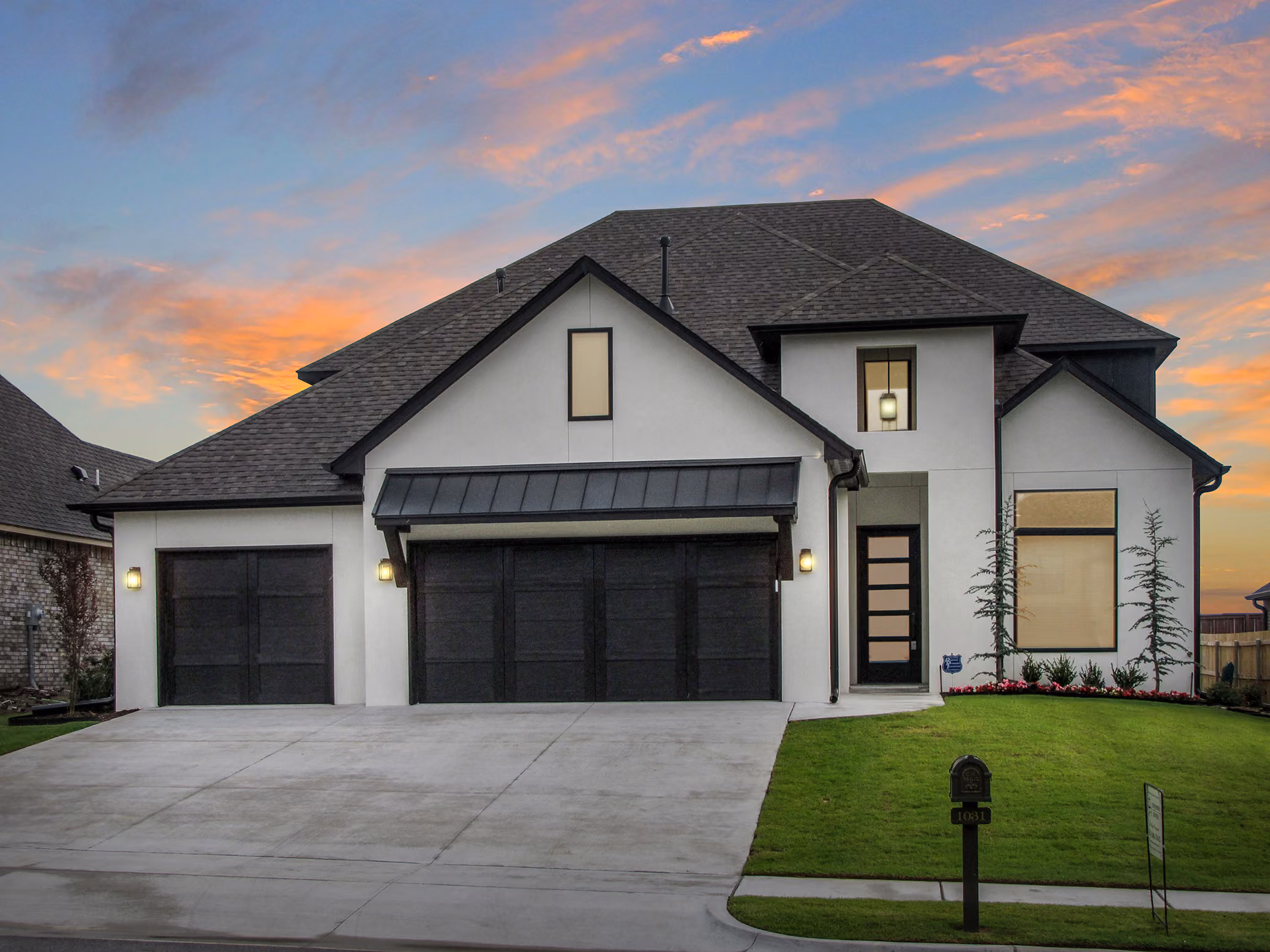 Modern two-story house with white exterior, black garage doors, and a front lawn under a colorful sunset sky.