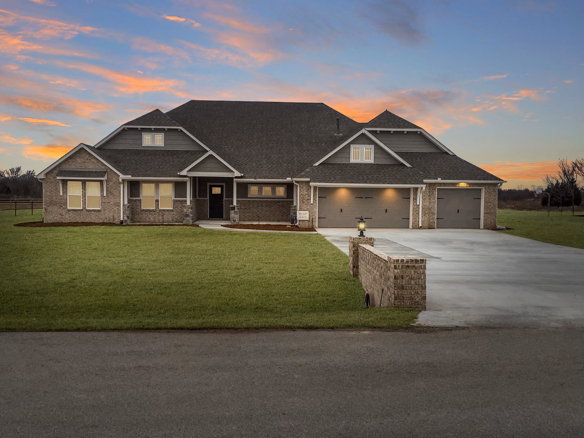 Large single-story brick house with a three-car garage, front lawn, and a sunset sky.
