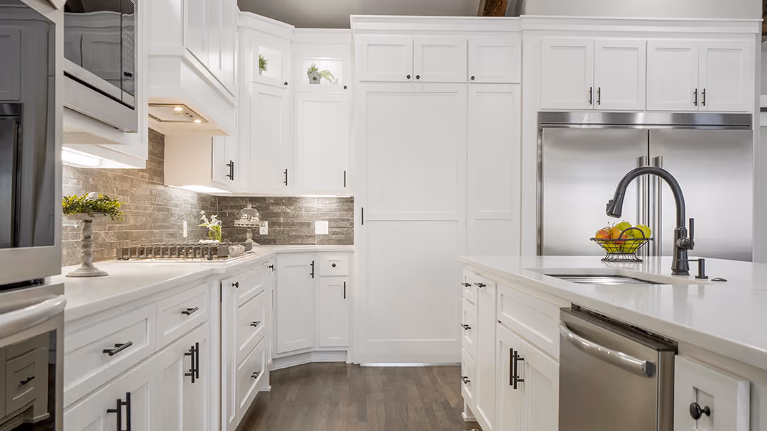 Modern kitchen with white cabinets, stainless steel appliances, a large island with sink and black faucet, and a bowl of fruit on the counter.