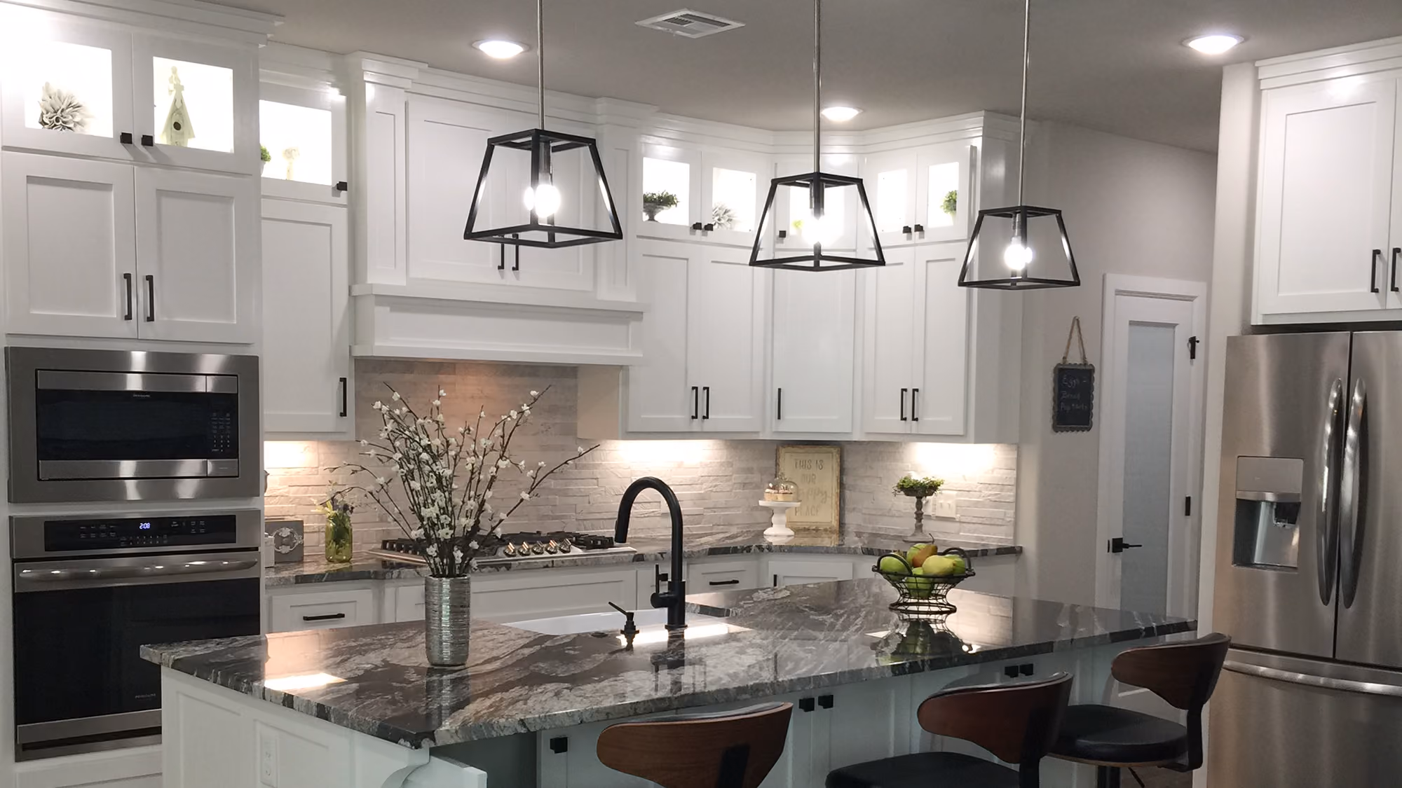 Modern kitchen with white cabinets, granite island, black pendant lights, and stainless steel appliances.