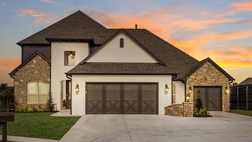 Modern two-story house with stone and stucco exterior, large driveway, and three garage doors at sunset.