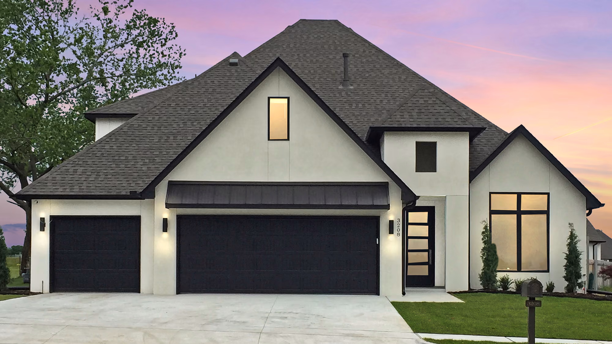 Modern two-story house with gray roof, two black garage doors, tall narrow window above garage, and black-framed large windows under a purple and orange sunset sky.