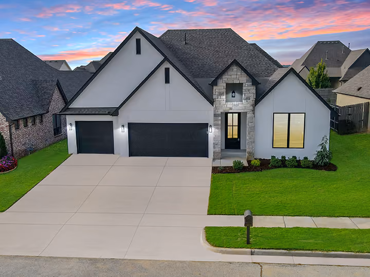 Modern single-story house with gray exterior, black garage doors, and landscaped front lawn at sunset.