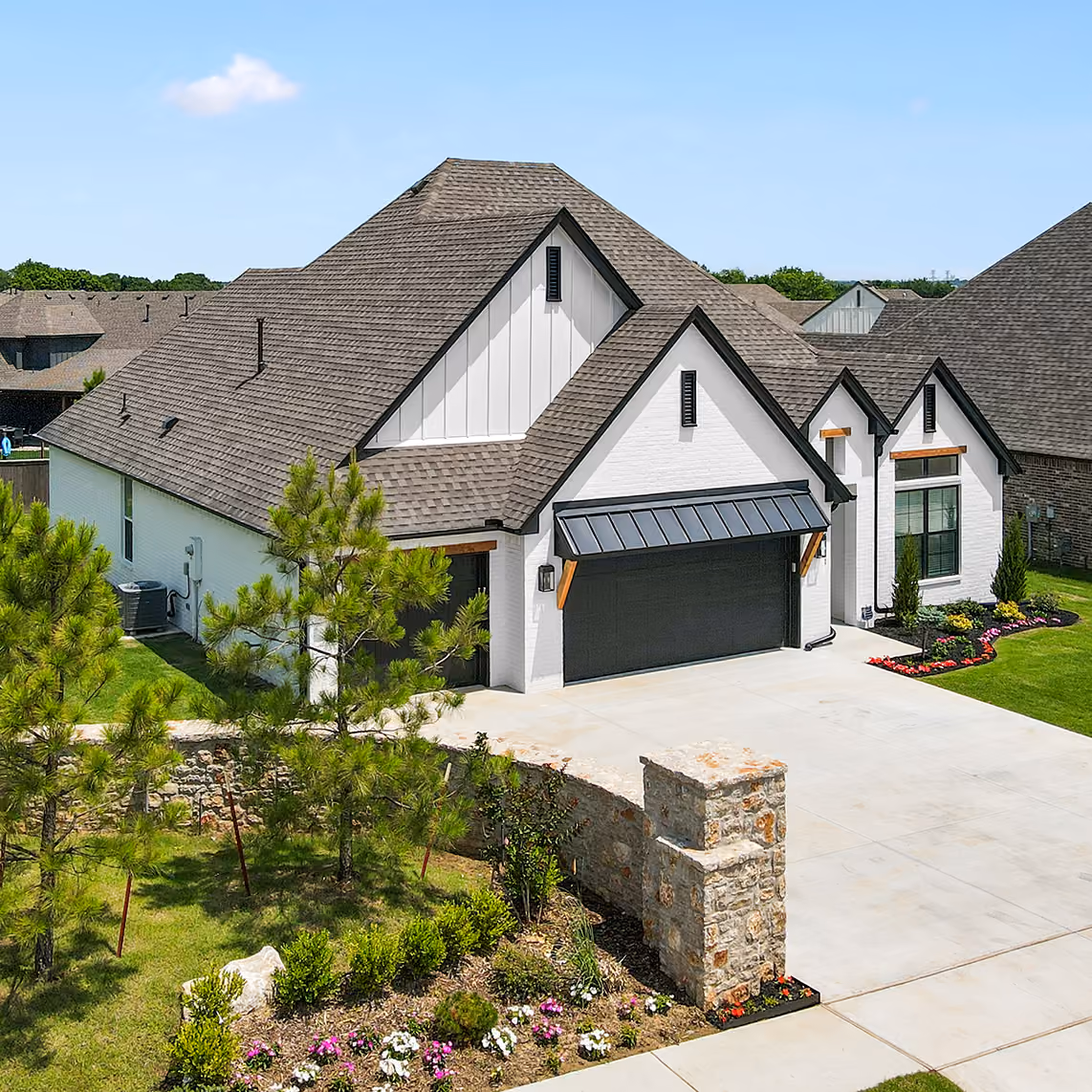 Modern white house with dark roof, black garage door, and landscaped yard with small trees and flowers.