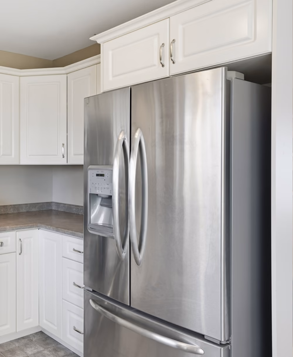 Stainless steel French door refrigerator with water dispenser in a white kitchen corner.