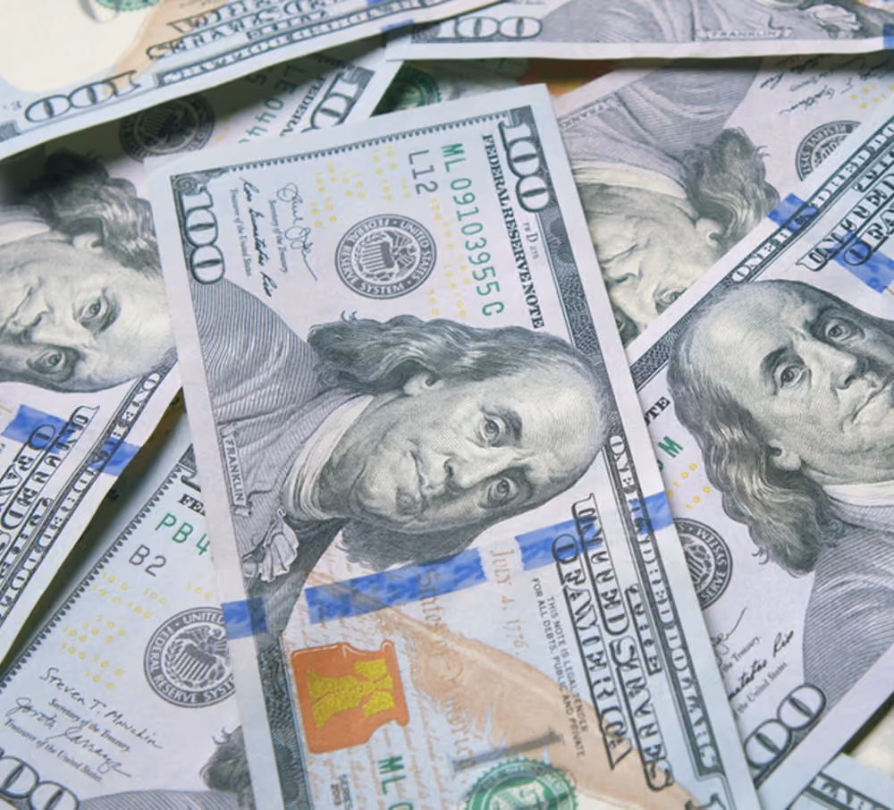 Close-up of several overlapping U.S. 100 dollar bills showing Benjamin Franklin's portrait.