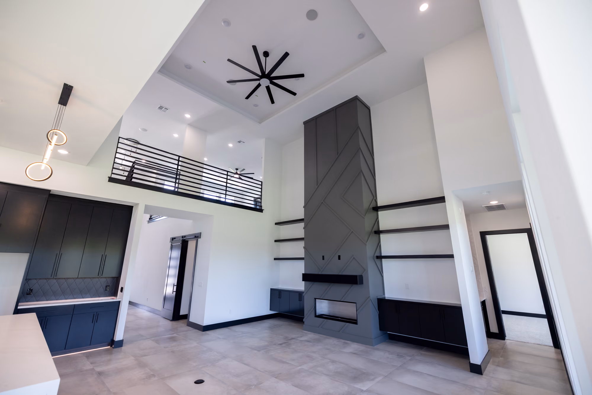 Modern open living room with high ceiling, black fireplace, shelves, and second-story black railing.