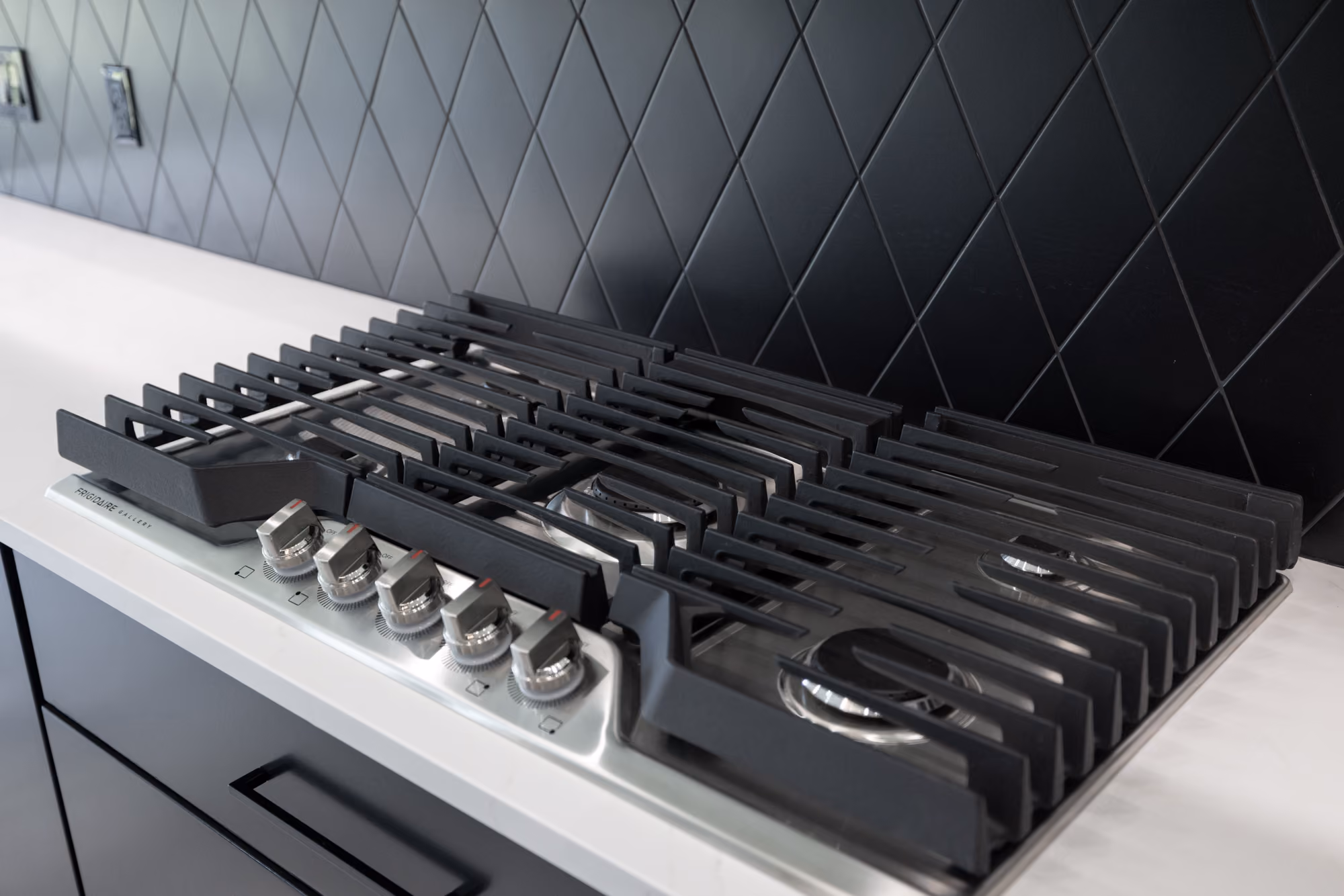 Stainless steel Frigidaire gas cooktop with five burners and black grates on a white countertop.