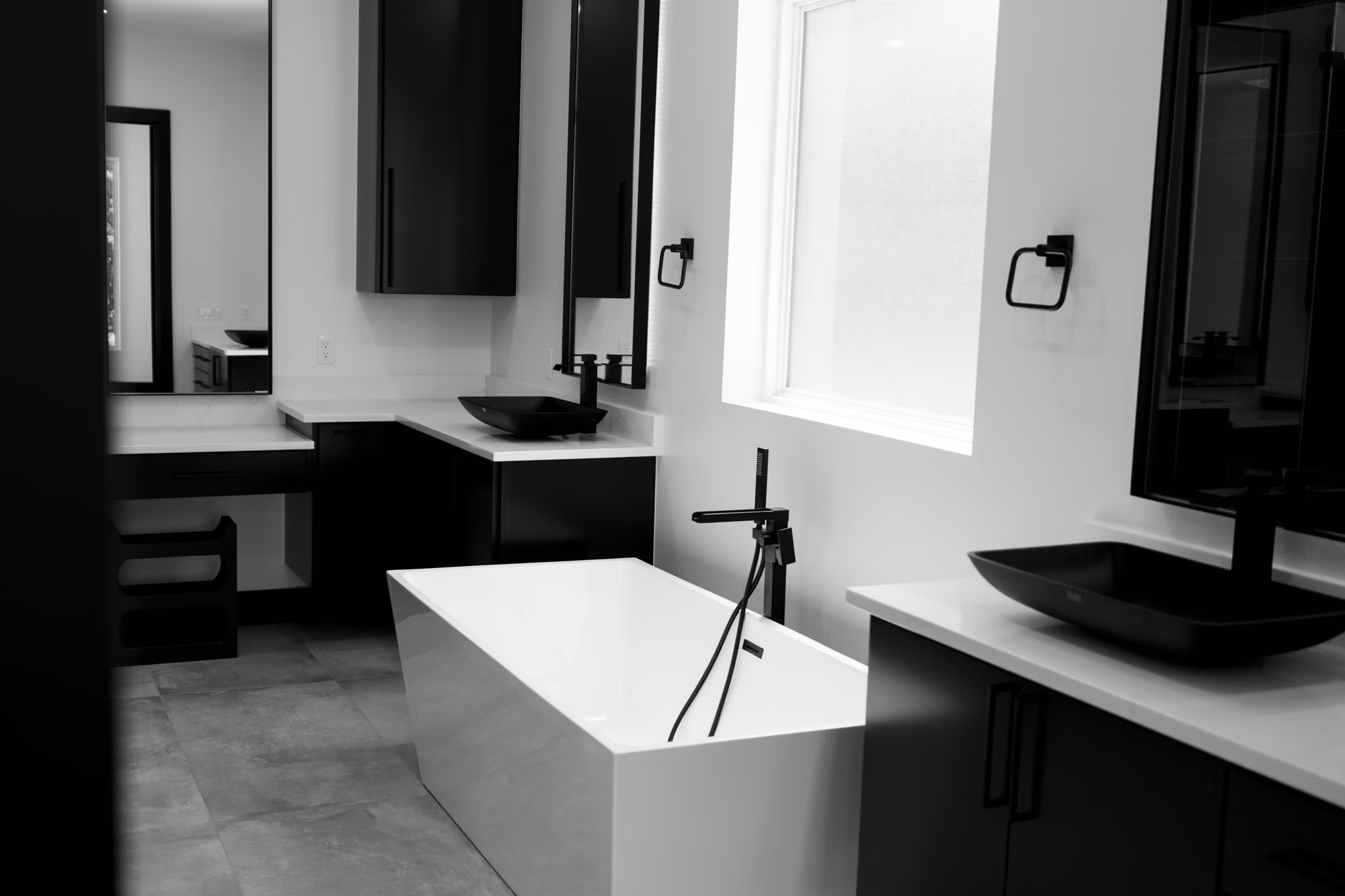Modern bathroom with freestanding bathtub, black vessel sinks, and dark cabinetry under white countertops.
