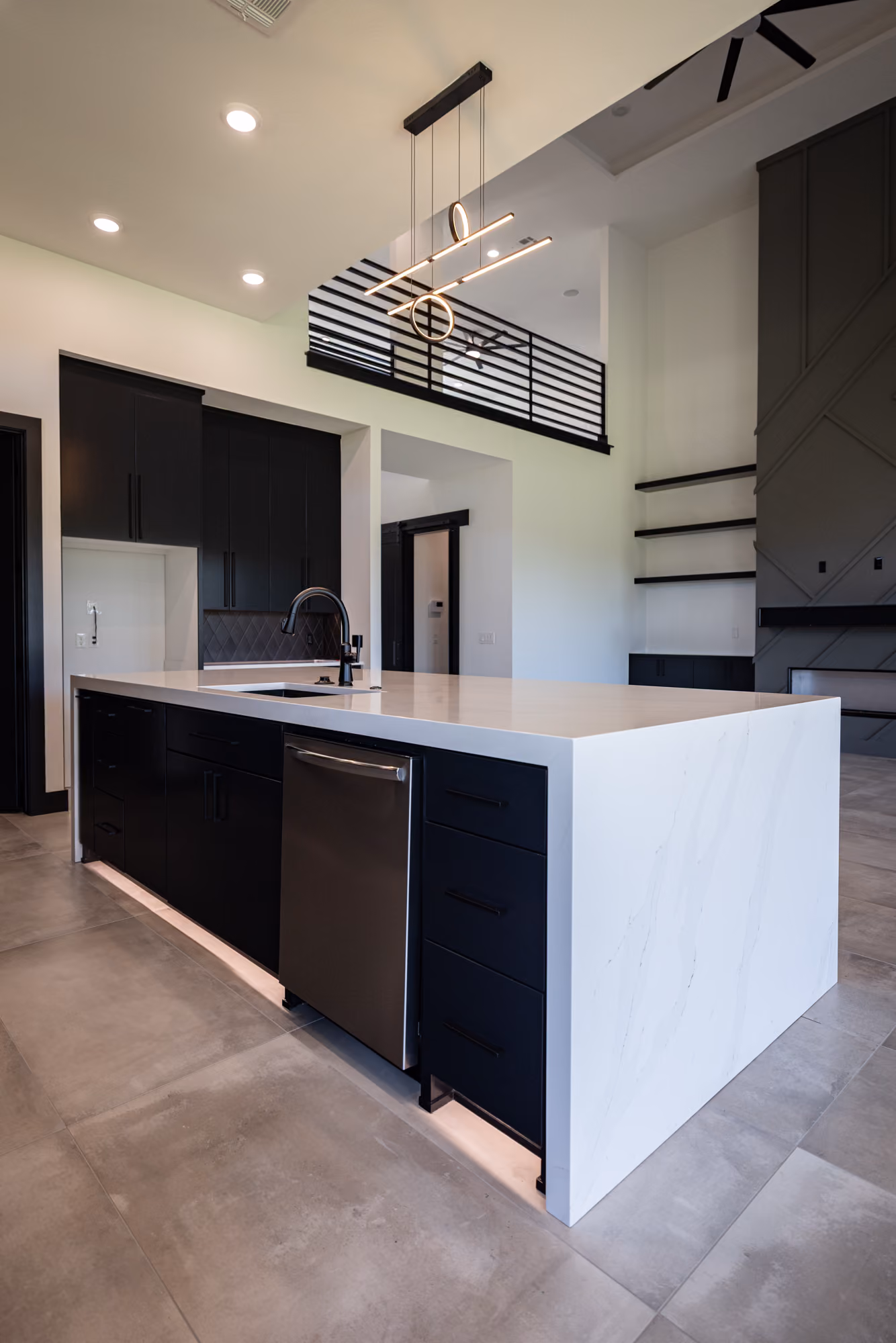 Modern kitchen with white marble island, black cabinetry, stainless steel dishwasher, and pendant light.