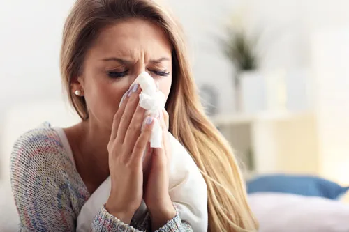 A woman blowing her nose while sitting on a couch.