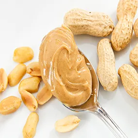 A spoon filled with peanut butter next to peanuts.
