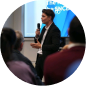 Man speaking with a microphone in front of an audience in a conference setting.