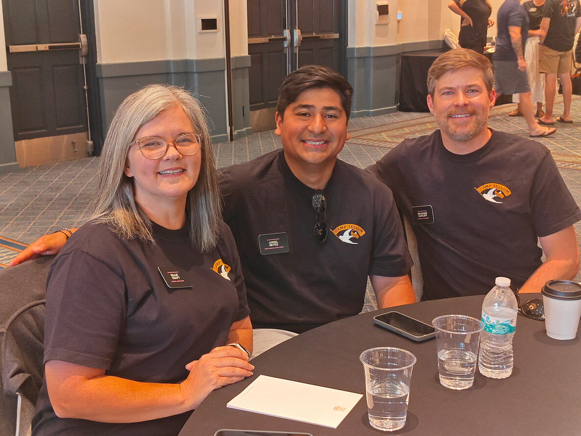 Group of people smiling and posing together at an outdoor table.