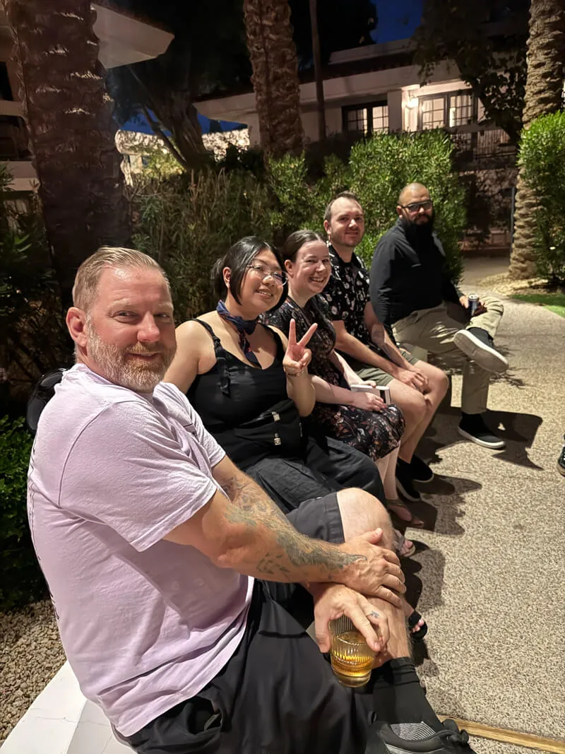 Five people sitting on a bench outside at night, smiling and posing for the photo, with one person making a peace sign.