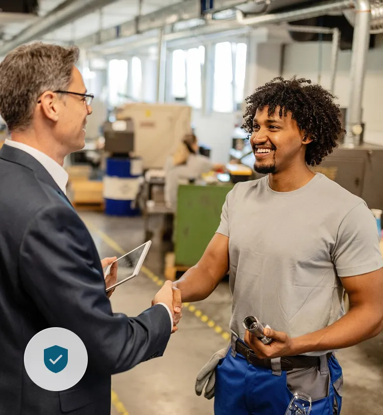 Ingenieur und Arbeiter geben sich Handschlag in Fabrikumgebung.