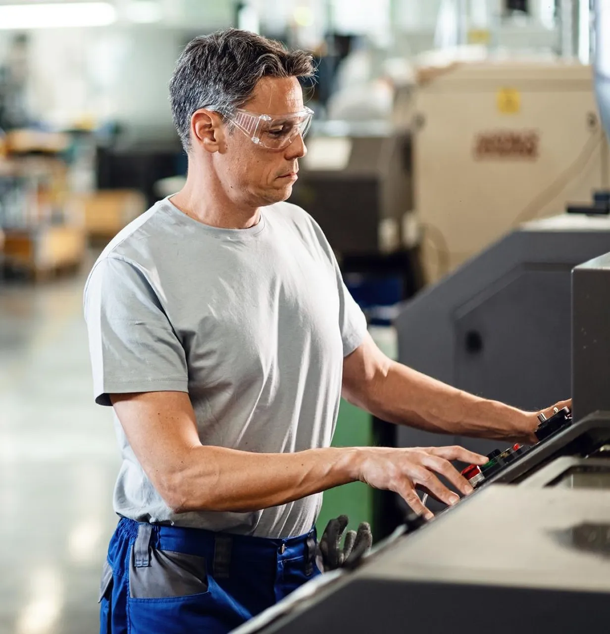 Arbeiter bedient Maschine mit Schutzbrille in Werkhalle.