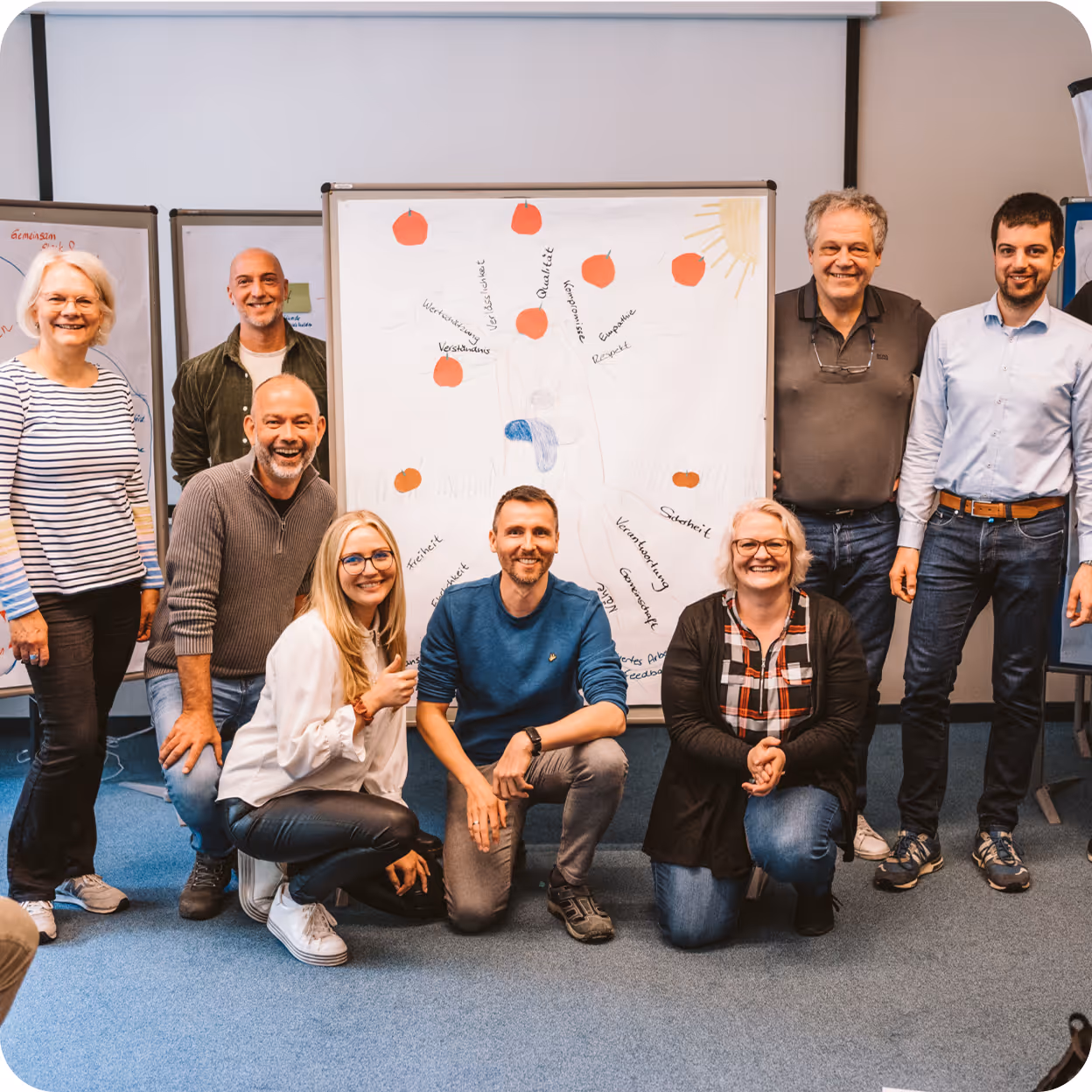 Eight people smiling and posing in front of a whiteboard with red apple drawings and handwritten words in a meeting room.