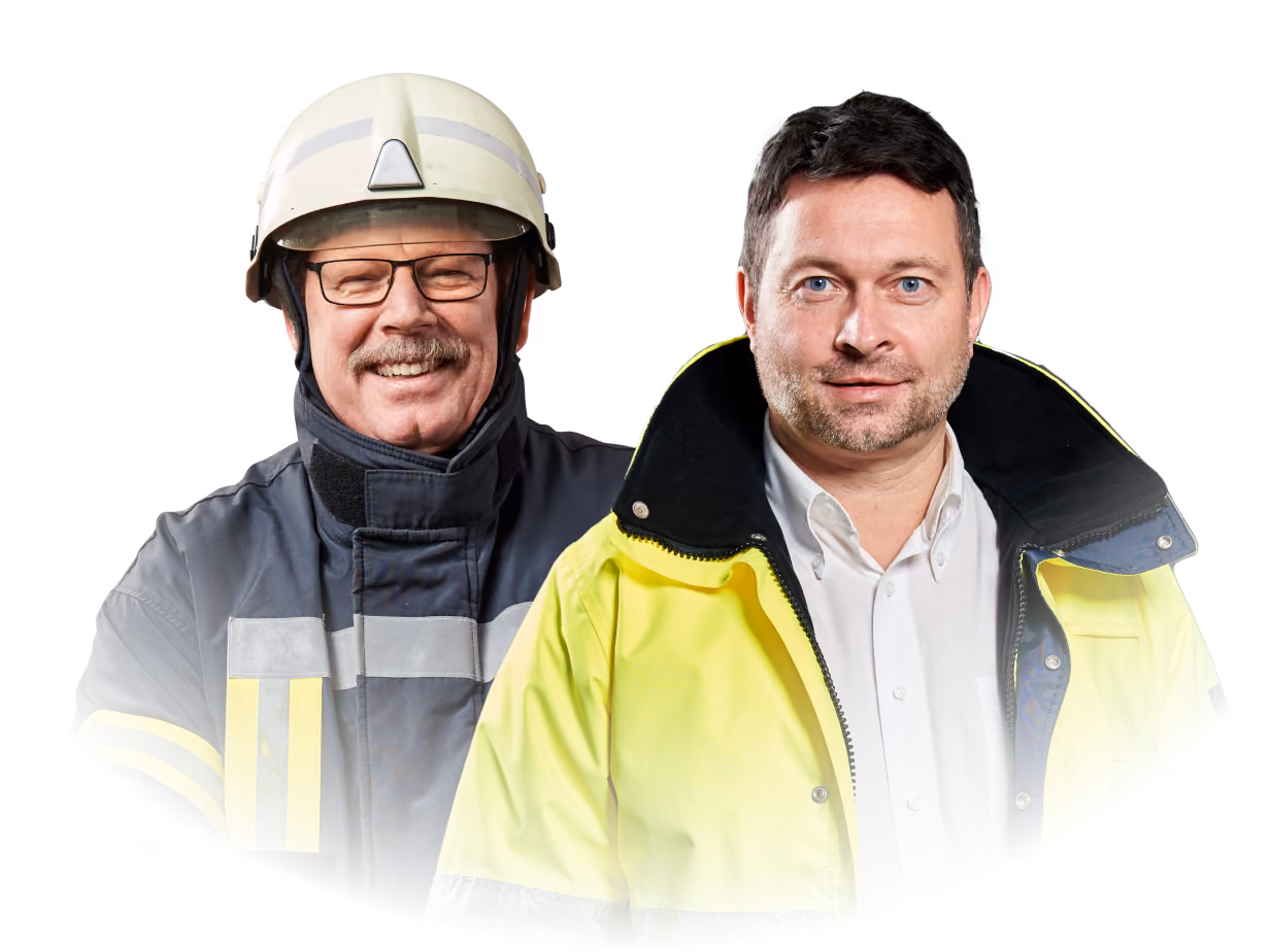 Zwei lächelnde Männer in Schutzkleidung: links Feuerwehrhelm und -jacke, rechts gelbe Warnjacke über Hemd