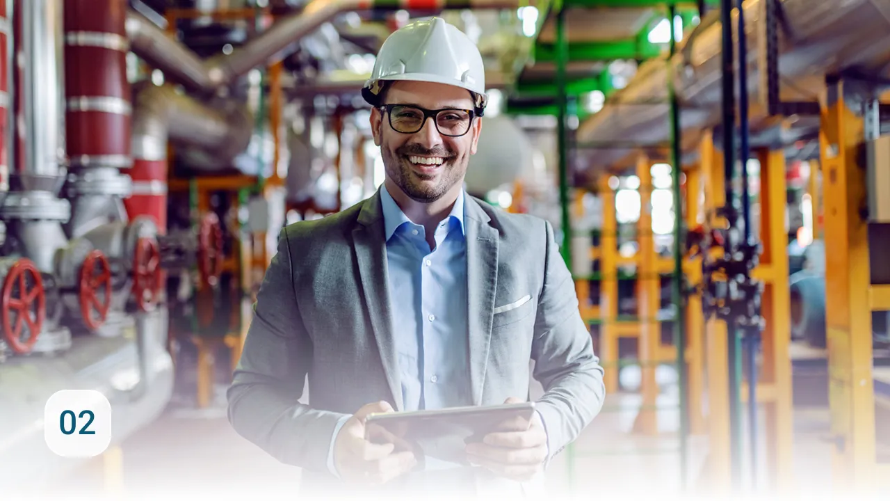 Ingenieur mit Schutzhelm und Tablet lächelt in einer Industrieanlage zwischen Rohren und Ventilen
