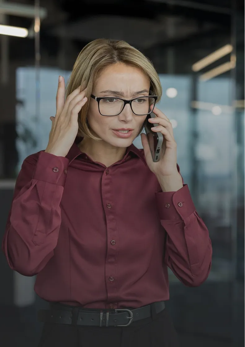 Frau mit Brille in roter Bluse wirkt besorgt, spricht nervös am Handy in modernem Büro