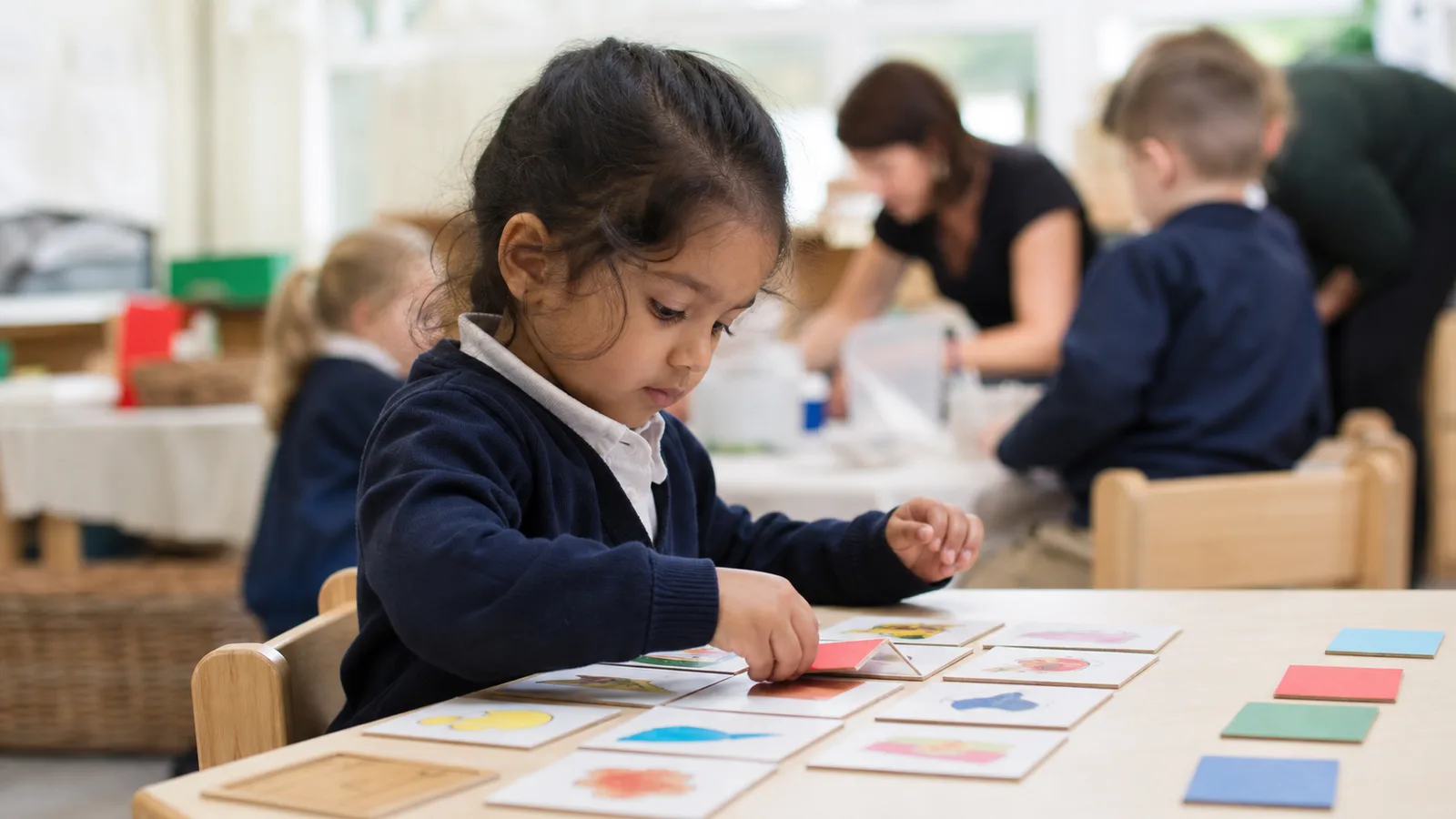 An early-years child matching a coloured card to a picture at a low table