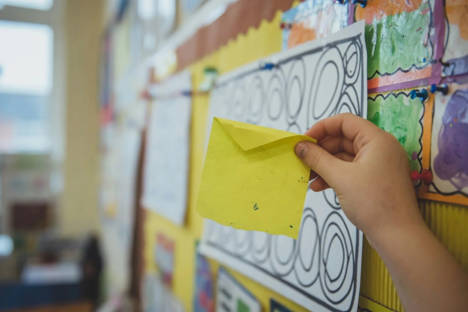 Key Stage 2 learner takes a sticky note from an English working wall, the modelled writing soft in the background