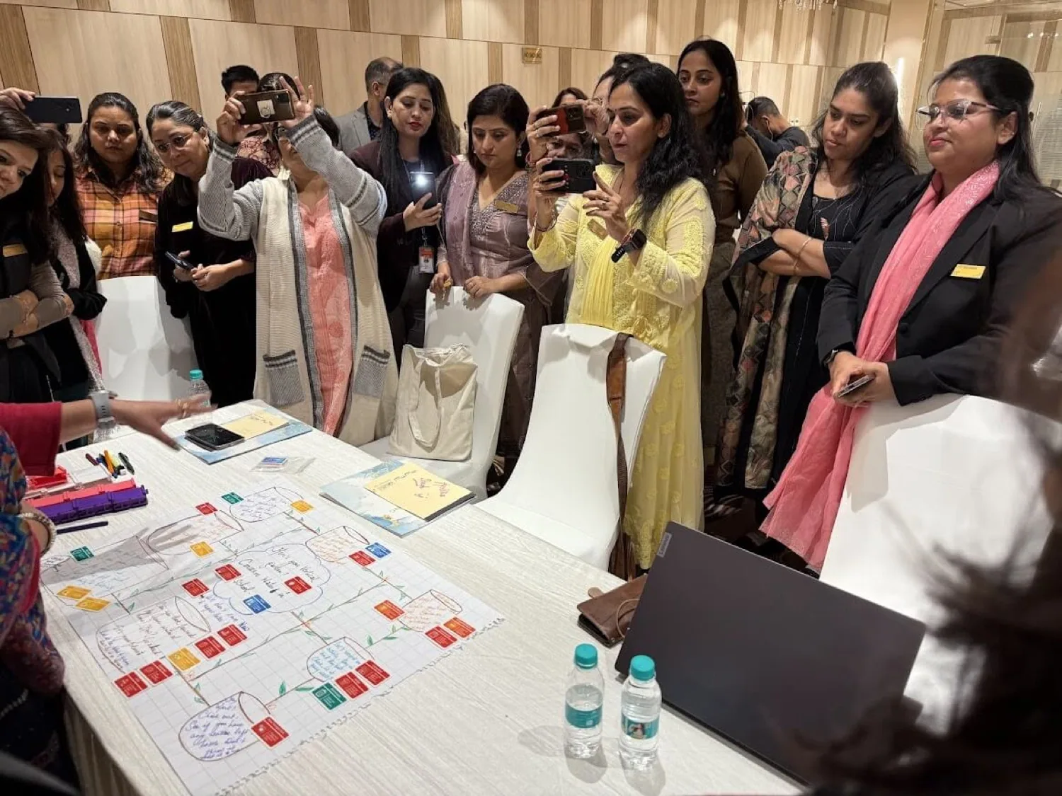Teachers crowding round a table to photograph a learning journey they have drawn, at a conference outside Delhi.
