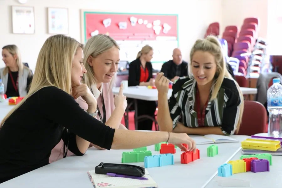 Three teachers leaning over a table of coloured blocks in a staff session.