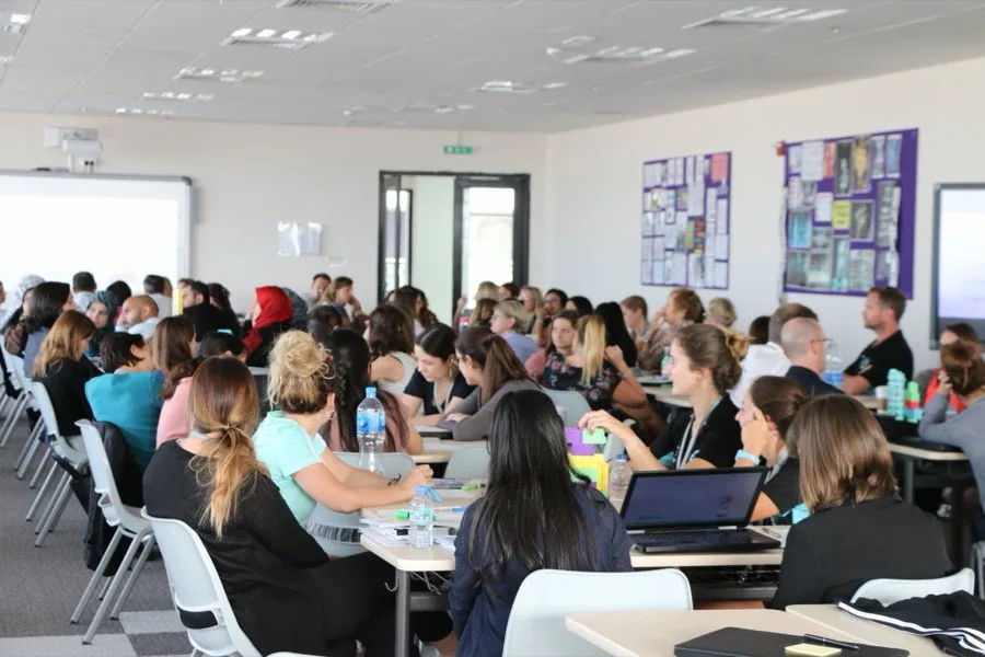 A full training room of teachers at round tables.