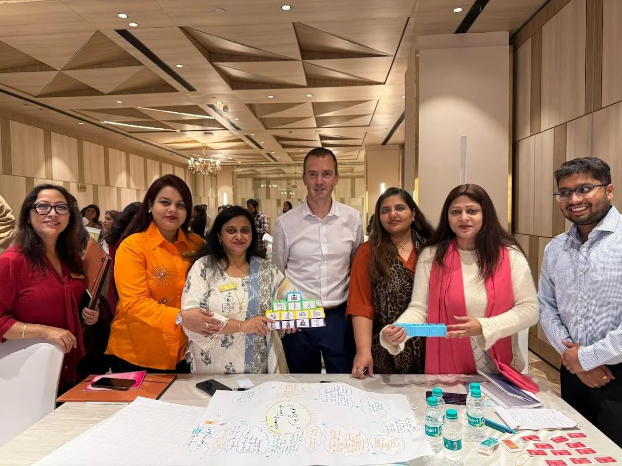 Paul Main with a team of teachers in Delhi, holding the blocks they have just built over the plan they drew for it