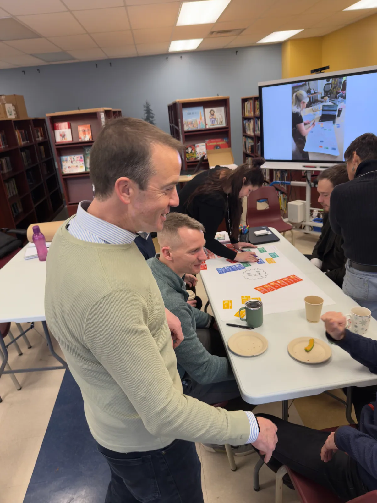 Paul Main shaking hands with a teacher at a planning table in a school library in Quebec, Thinking Framework cards on the table