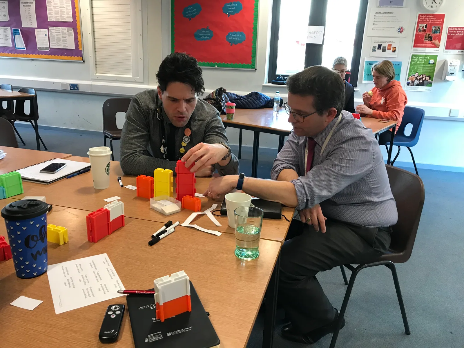 Two teachers at a classroom table building a structure from red, yellow and white Writer's Block blocks.