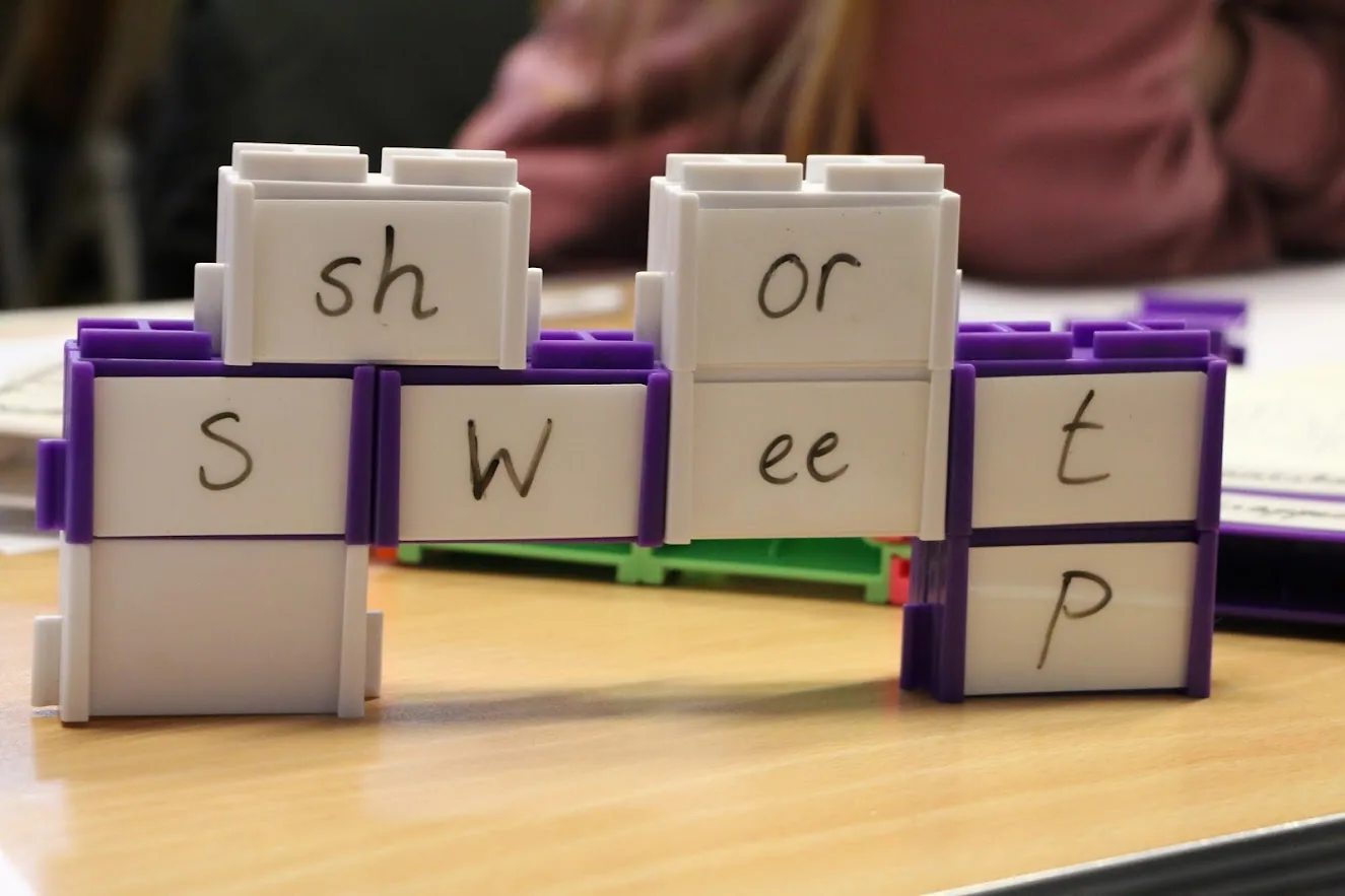 Blocks with handwritten sounds on their panels, sh, or, s, w, ee, t, p, stacked to build words