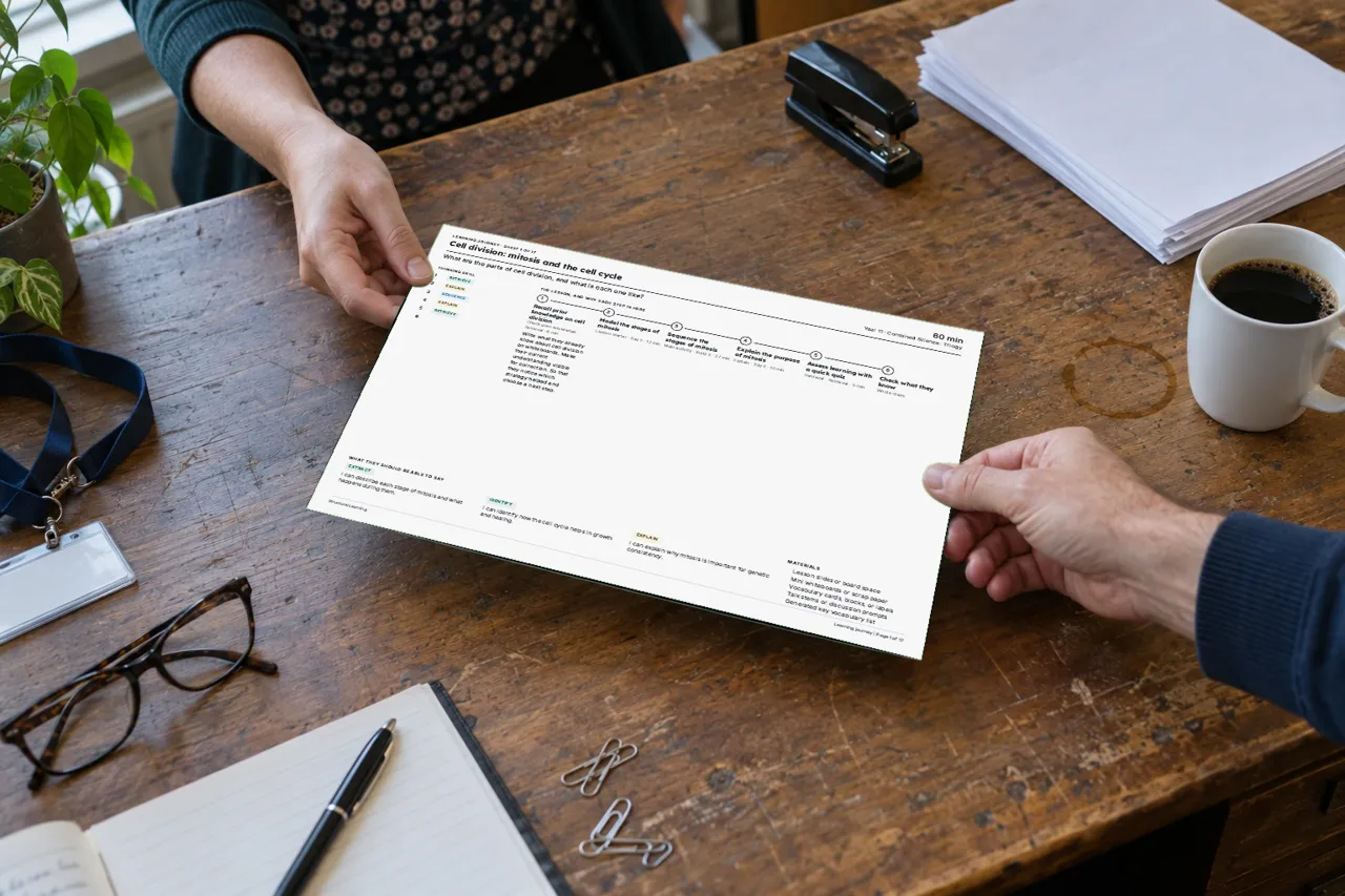 One teacher hands a colleague a printed page across a staff room desk: the real first page of a lesson pack from the platform, the learning journey.
