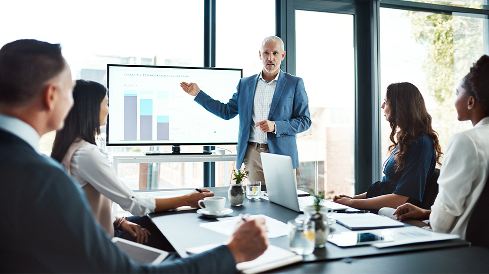 Business advisor presenting a chart on a screen to a group of colleagues in a meeting room.