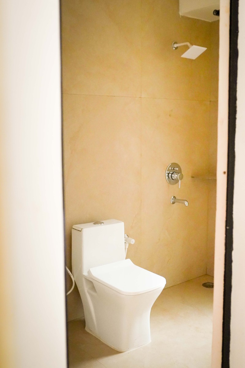 Minimalist bathroom with white toilet and wall-mounted showerhead on beige tiled walls.