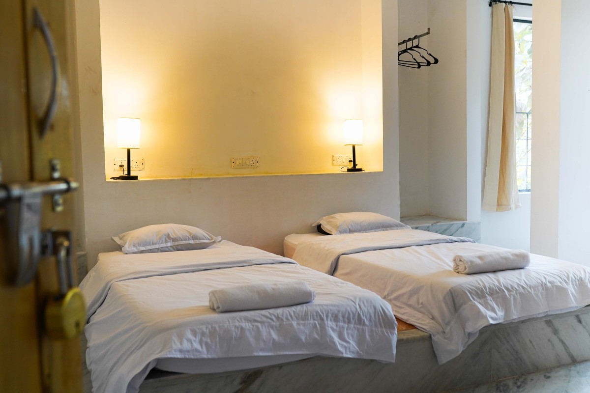 Minimalist room with two single beds, white linens, rolled towels, and soft wall lamps.