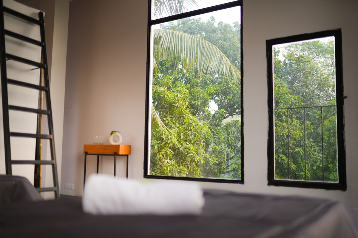 Interior with large windows showing green trees, a black ladder, and a small wooden table with decor.