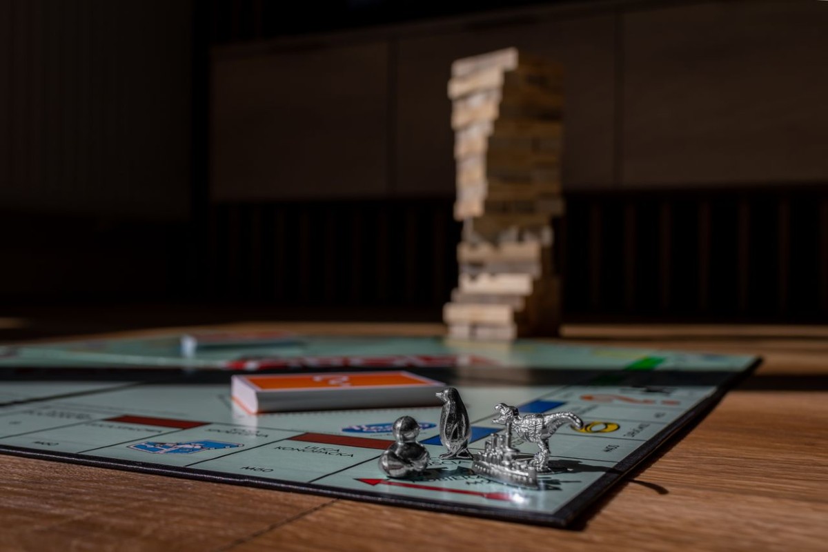 Close-up of Monopoly board with metal game tokens and a blurred wooden block tower in the background.
