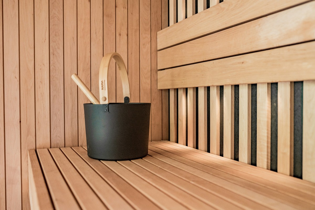 Black sauna bucket with wooden handle on a wooden bench in a sauna room.