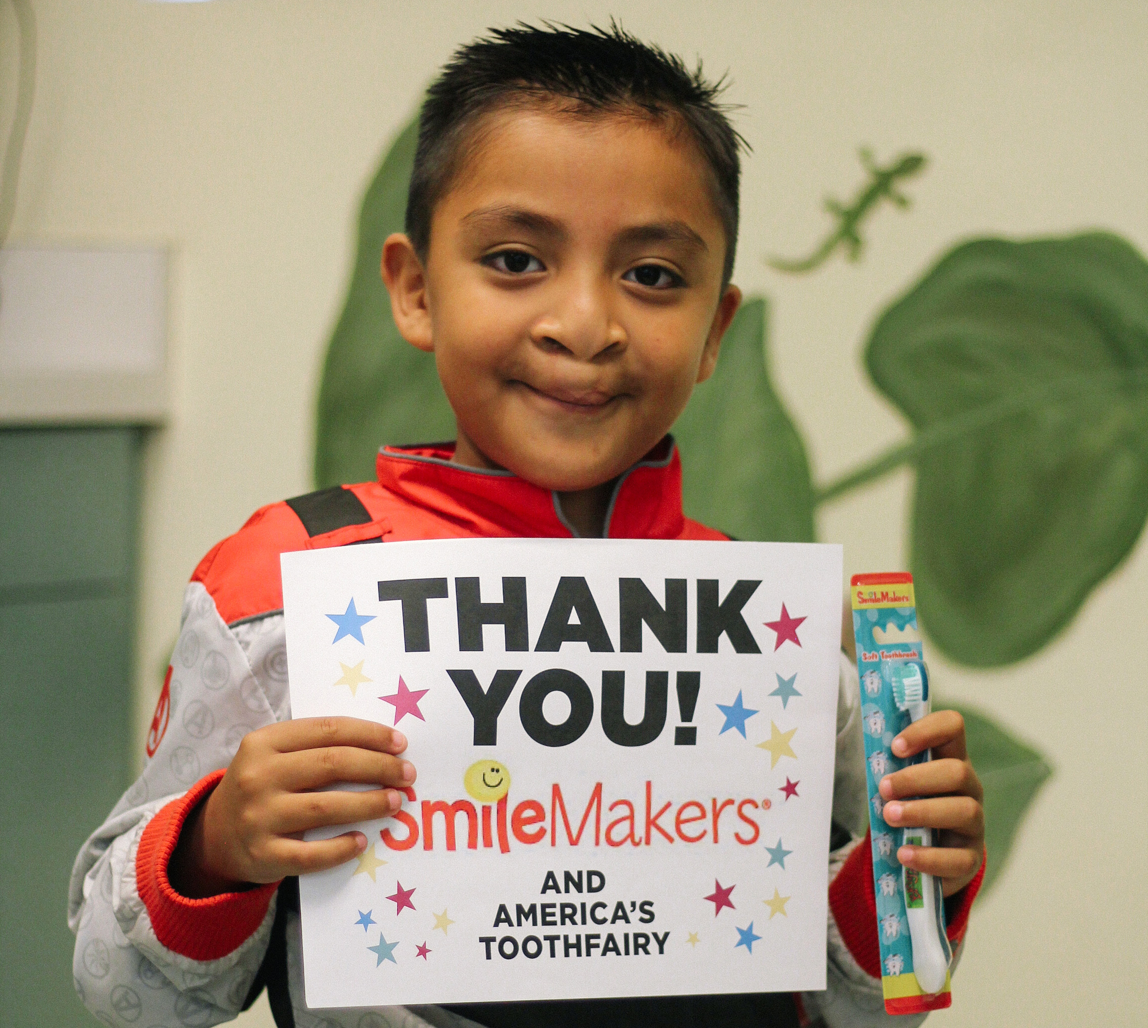 Boy with toothbrush holds up thank you sign for Smile Makers