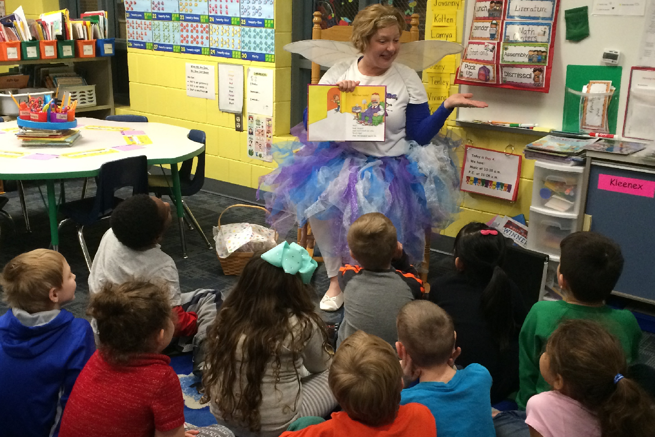 The Smile Fairy displays the book "The Tooth Book" while reading it to students.