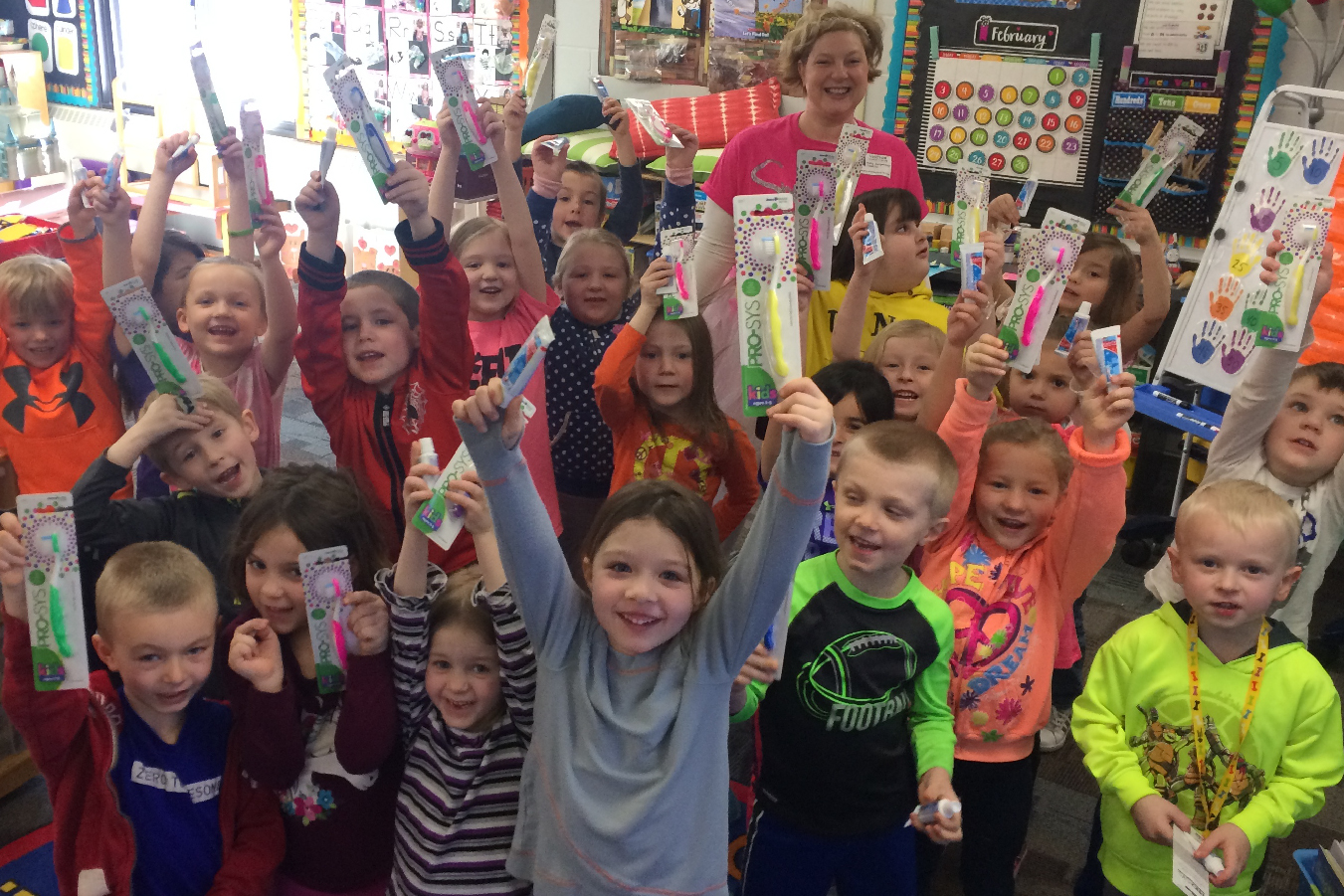 A group of children smile and show the toothbrushes and toothpaste they received from the Smile Fairy.