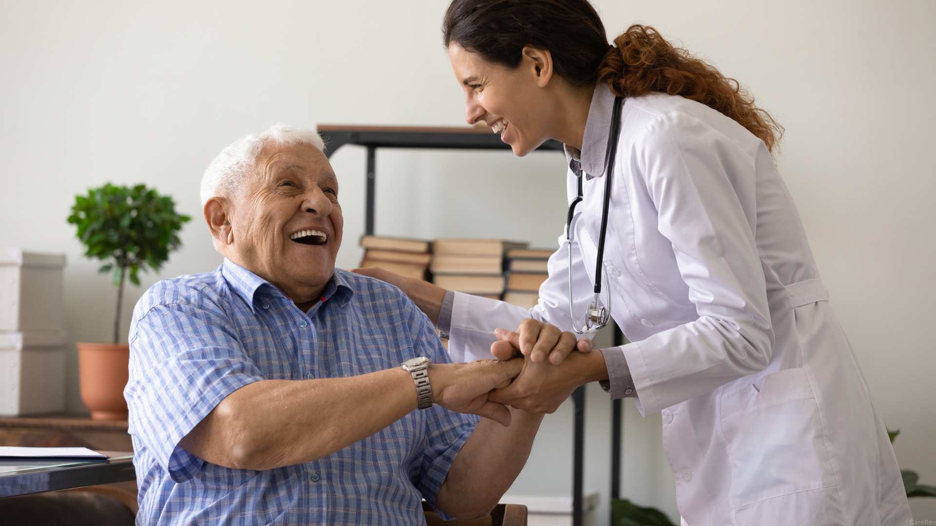 A doctor greets her elderly patient with a small and embracing his hands.