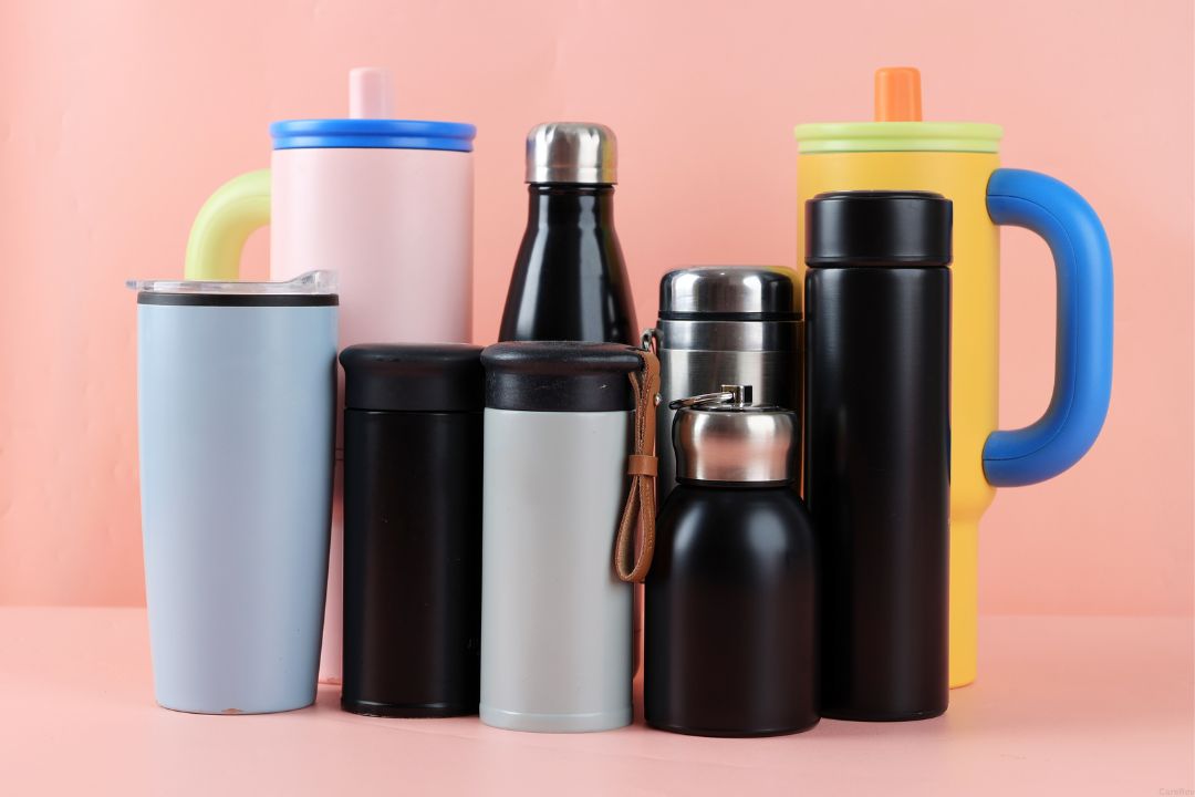 A group of various insulated water bottles in front of a pink background.