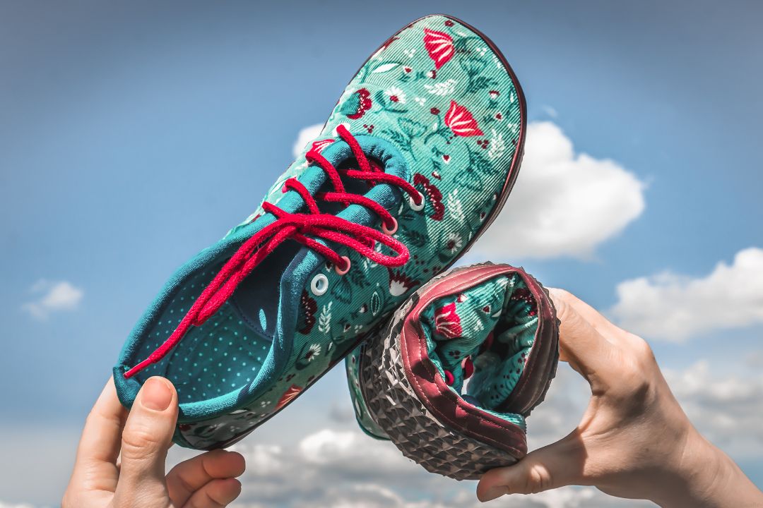 Colorful barefoot shoes with a wide toe box held up against the sky.