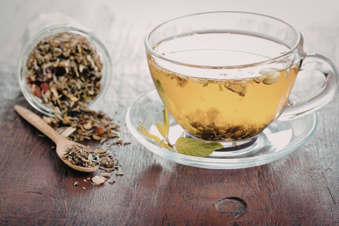 Loose tea leaves next to a glass of herbal tea in a clear teacup.