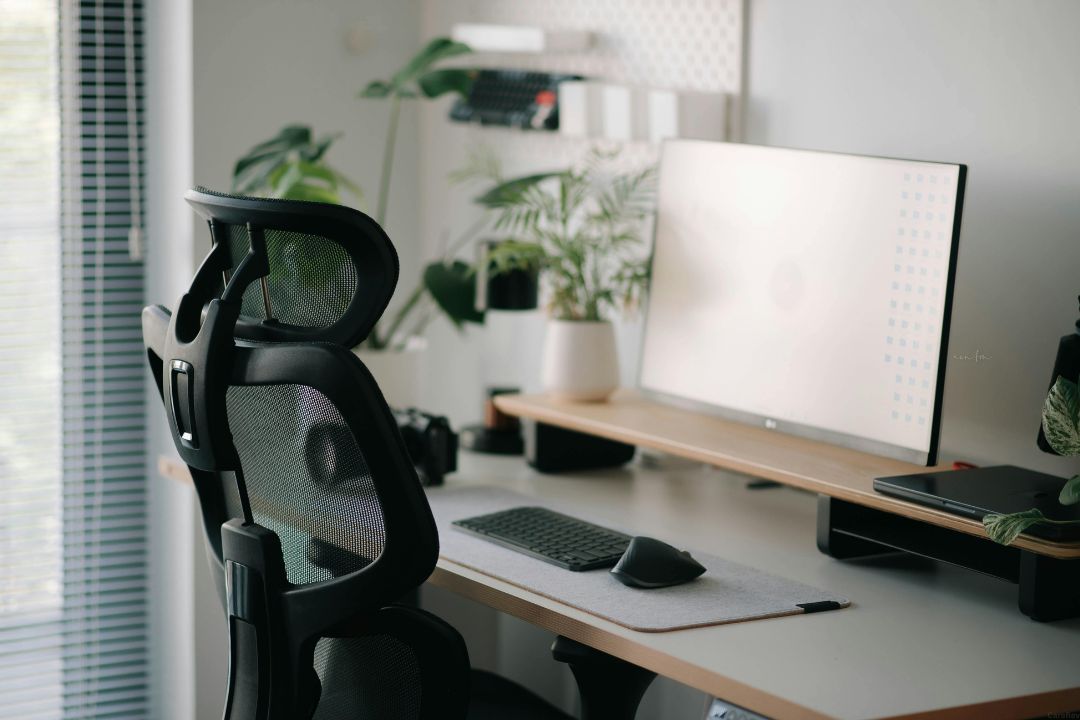 An ergonomical desk chair sits in front a desk and computer screen.