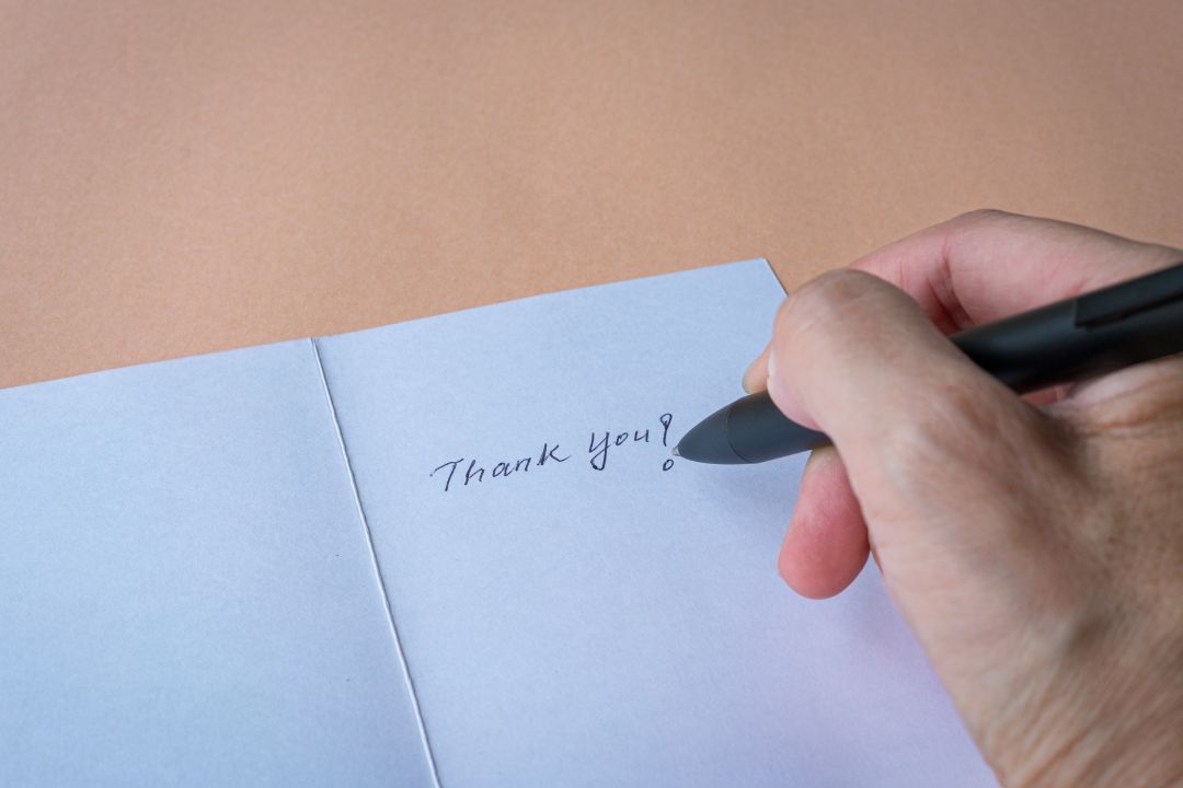 A hand writing a card that says "Thank You!"
